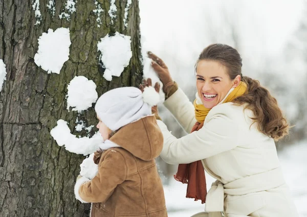 Счастливая мать и ребенок делают лицо для дерева из снега — стоковое фото