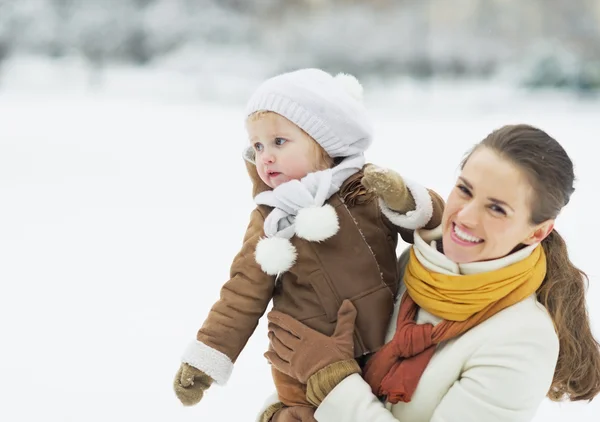 Szczęśliwą matką gospodarstwa dziecko patrząc na miejsce w winter park — Zdjęcie stockowe