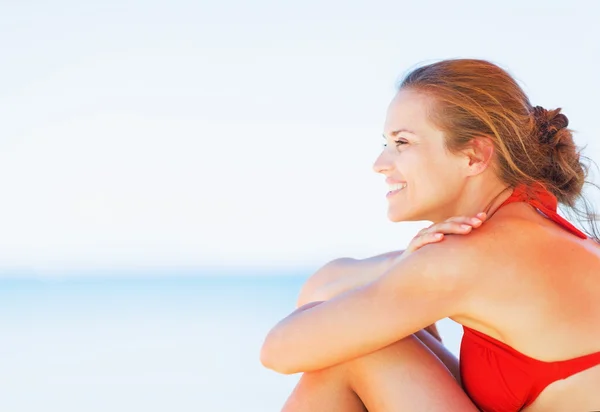 Gelukkig jonge vrouw zittend op het strand en op zoek op kopie ruimte — Stockfoto