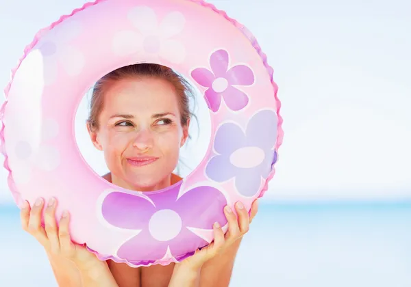 Thoughtful young woman on beach looking through swim ring on cop — Stock Photo, Image