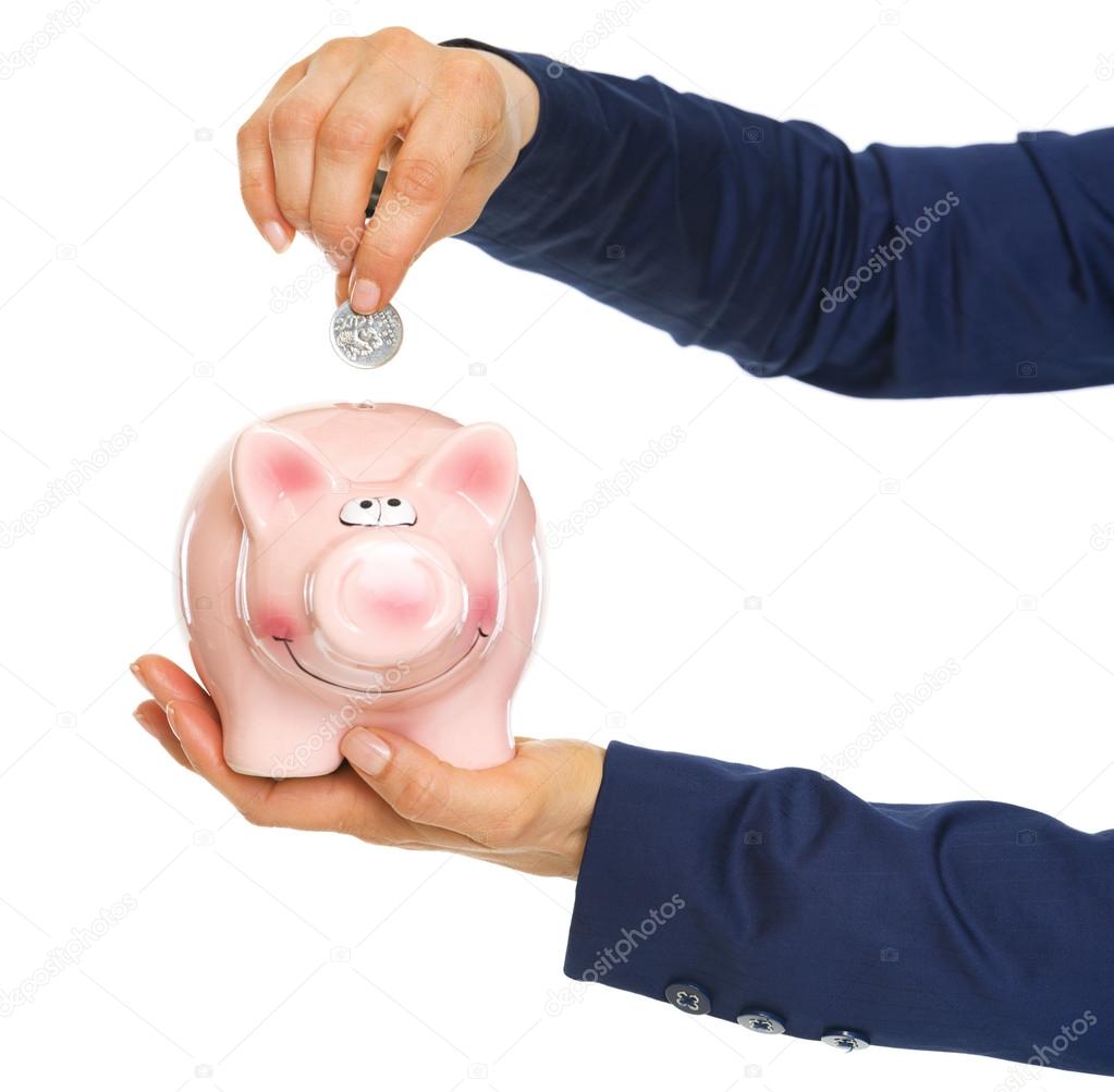 Closeup on business woman hands putting coin into piggy bank