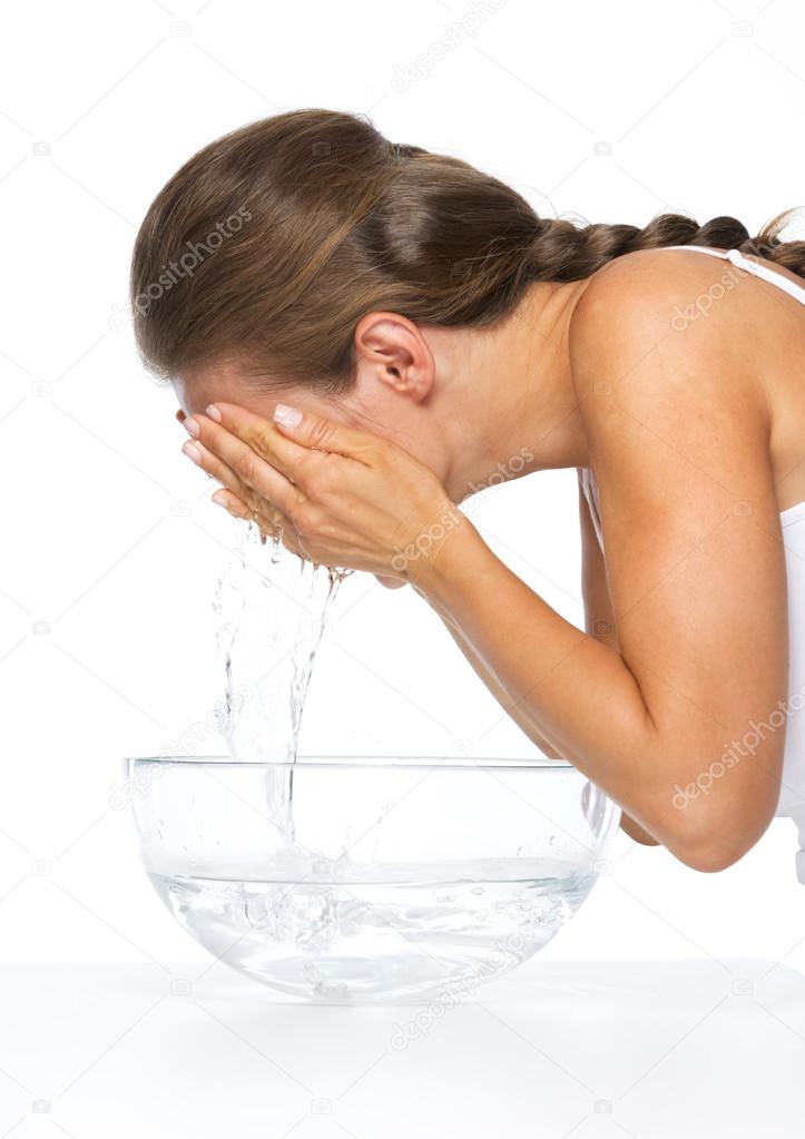 Young woman washing face in glass bowl with water