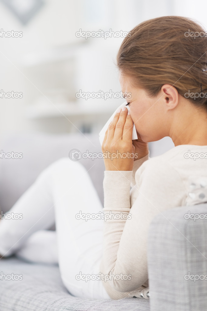Woman sitting on couch and blowing nose into handkerchief