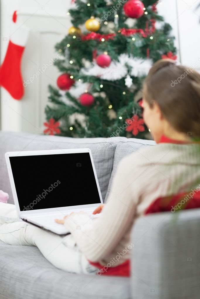 Young woman using laptop near christmas tree . rear view