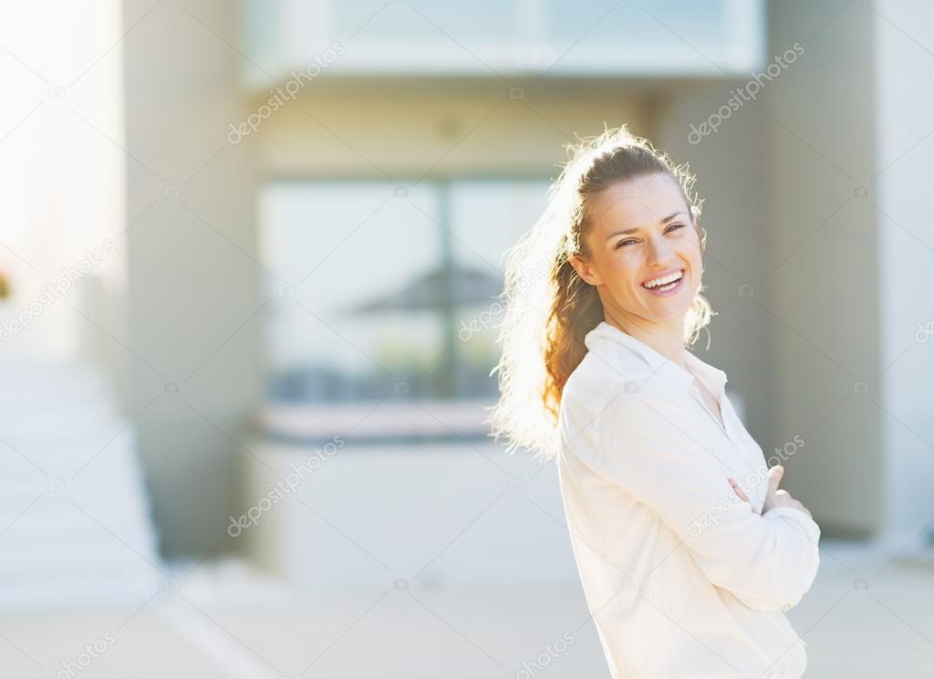 Portrait of happy young woman standing in front of house buildin