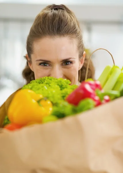 Junge Hausfrau versteckt sich hinter Einkaufstasche voller Gemüse — Stockfoto