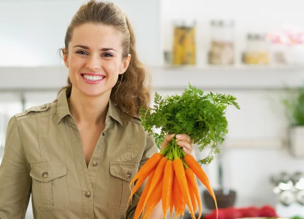 Feliz joven ama de casa sosteniendo montón de zanahorias en la cocina — Foto de Stock