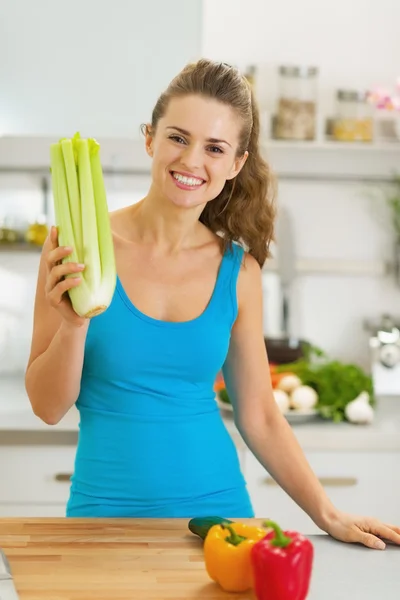 Lachende jonge vrouw met selderij in moderne keuken — Stockfoto