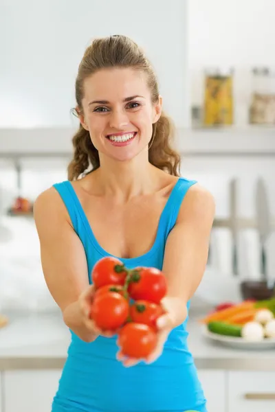 Mujer joven sonriente mostrando un montón de tomate en la cocina moderna — Foto de Stock
