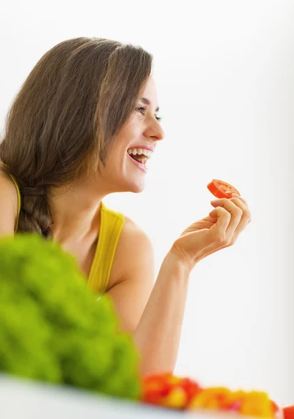 Sorridente giovane donna mangiare pomodoro in cucina — Foto Stock