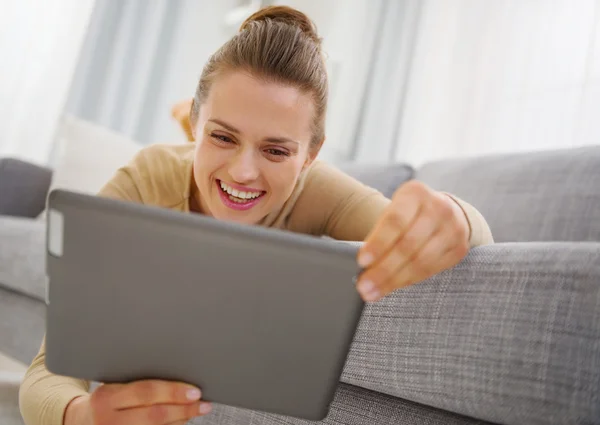 Mujer joven sonriente usando tableta PC mientras está acostado en el sofá —  Fotos de Stock