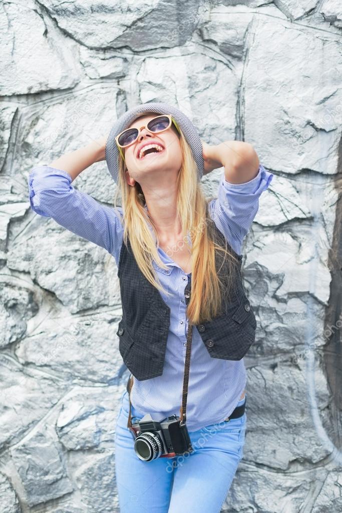 Happy hipster girl rejoicing against rocky wall outdoors