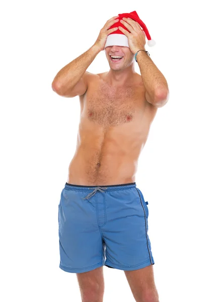 Smiling man in beach shorts pulling santa hat over eyes — Stock Photo, Image