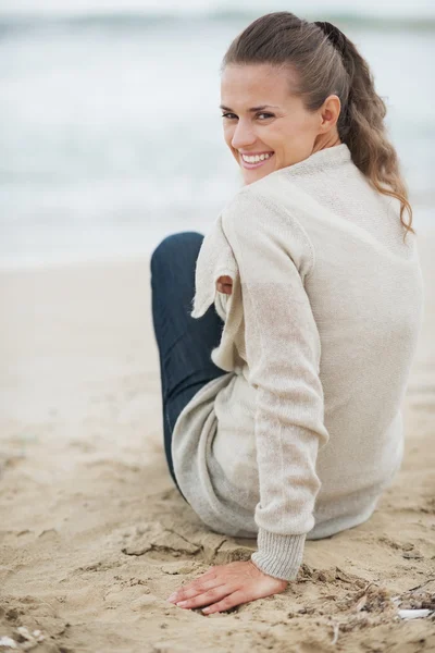 Glückliche junge Frau im Pullover sitzt am einsamen Strand — Stockfoto