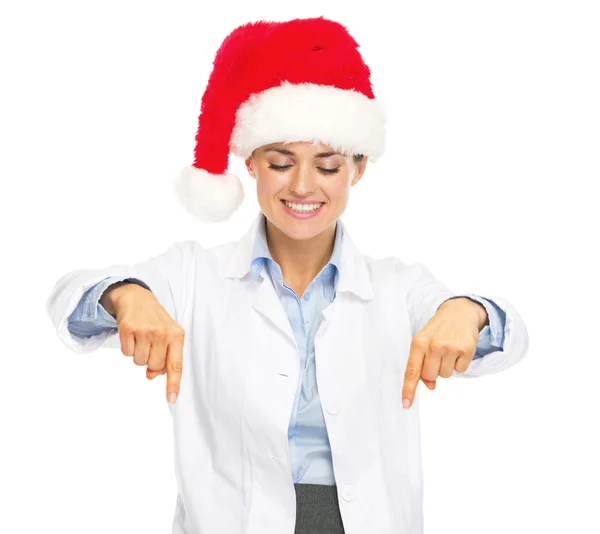 Femme médecin souriante dans le chapeau santa pointant vers le bas sur l'espace de copie — Photo
