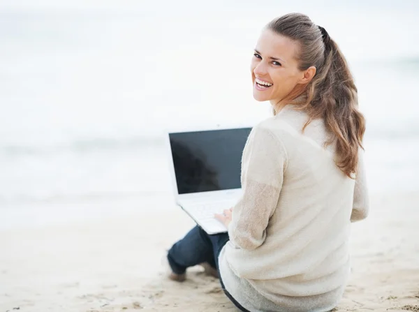 Mujer en jersey sentada en la playa con portátil —  Fotos de Stock