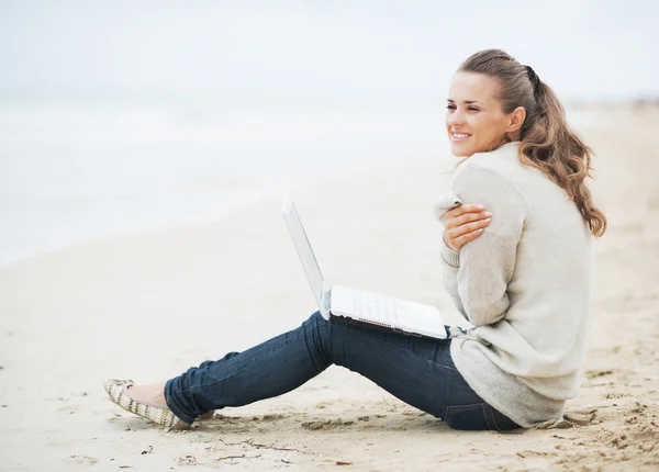 Frau im Pullover sitzt mit Laptop am Strand — Stockfoto