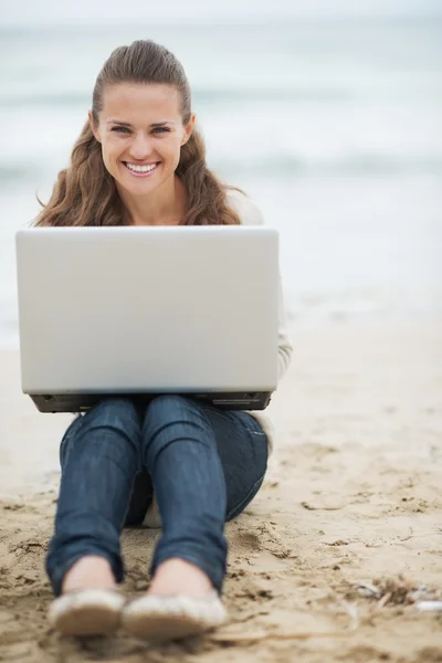 Femme en pull assis sur la plage avec ordinateur portable — Photo