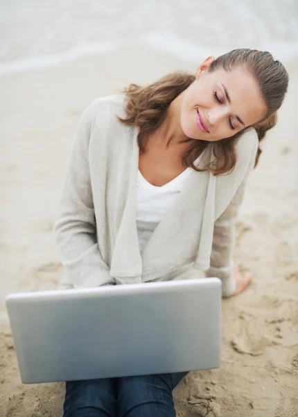 毛衣坐在海滩上的笔记本电脑上的女人 — 图库照片