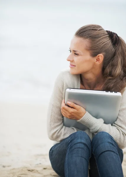 Kvinna i tröja sitter på stranden med laptop — Stockfoto