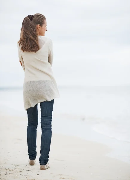 Mujer joven en suéter caminando en la playa solitaria —  Fotos de Stock