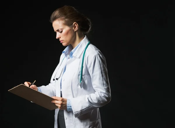 Sério médico mulher escrevendo em prancheta isolado em preto — Fotografia de Stock