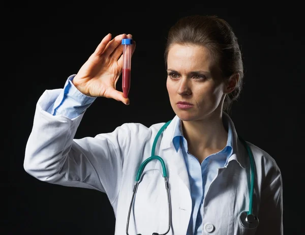 Ärztin schaut auf Reagenzglas auf schwarzem Hintergrund — Stockfoto