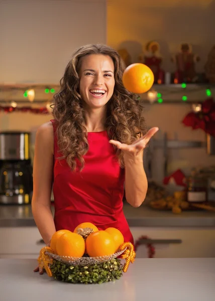 Smiling young woman throwing up orange in christmas decorated ki — Stock Photo, Image