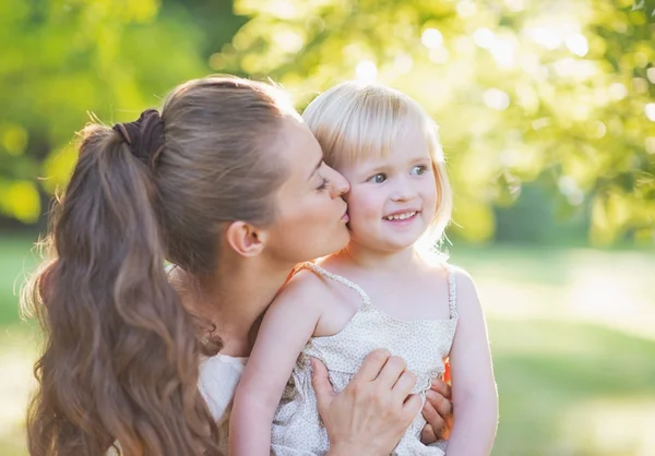 Portrét matka líbání baby venku — Stock fotografie