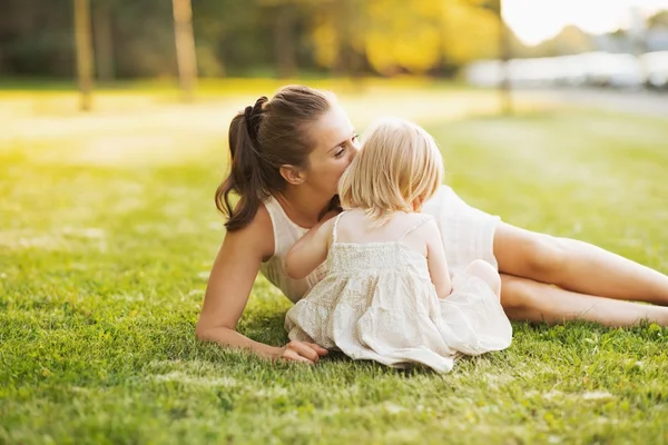 Mère embrasser bébé tout en étant assis sur la prairie dans le parc — Photo