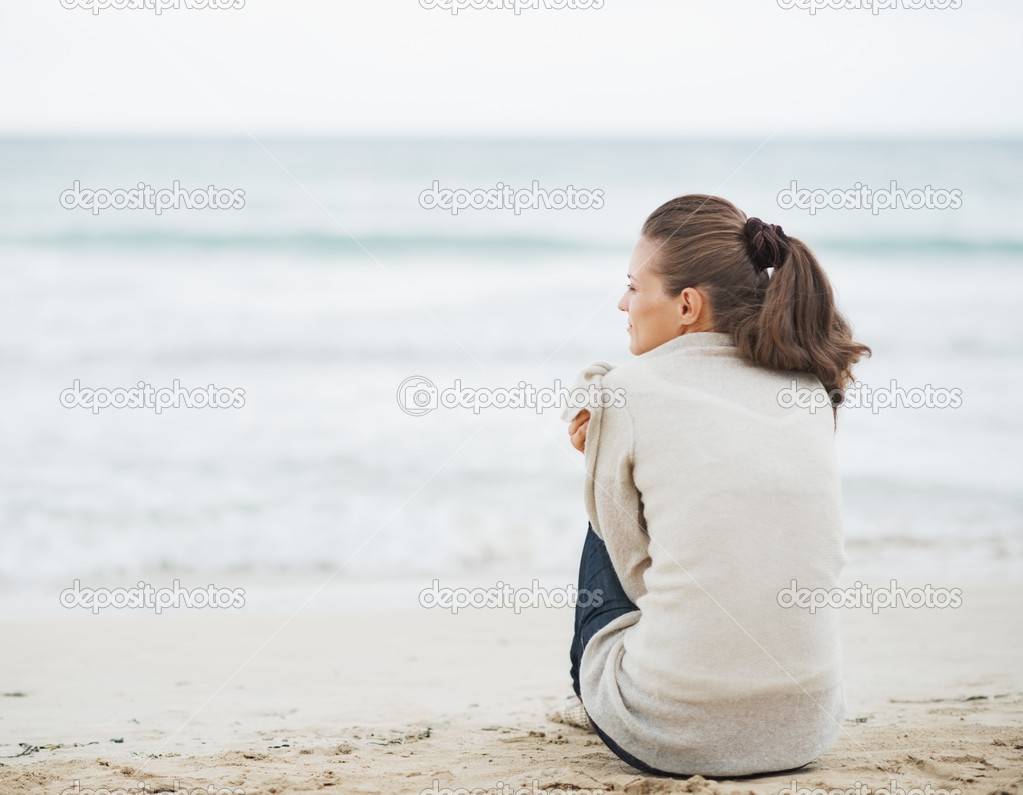 Young woman wrapping in sweater while sitting on lonely beach