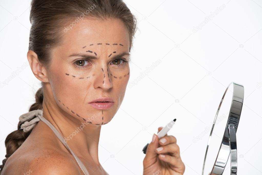 Woman with plastic surgery marks on face holding mirror and mark