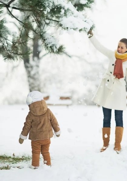 Happy mother and baby playing with snow on branch — Stock Photo, Image