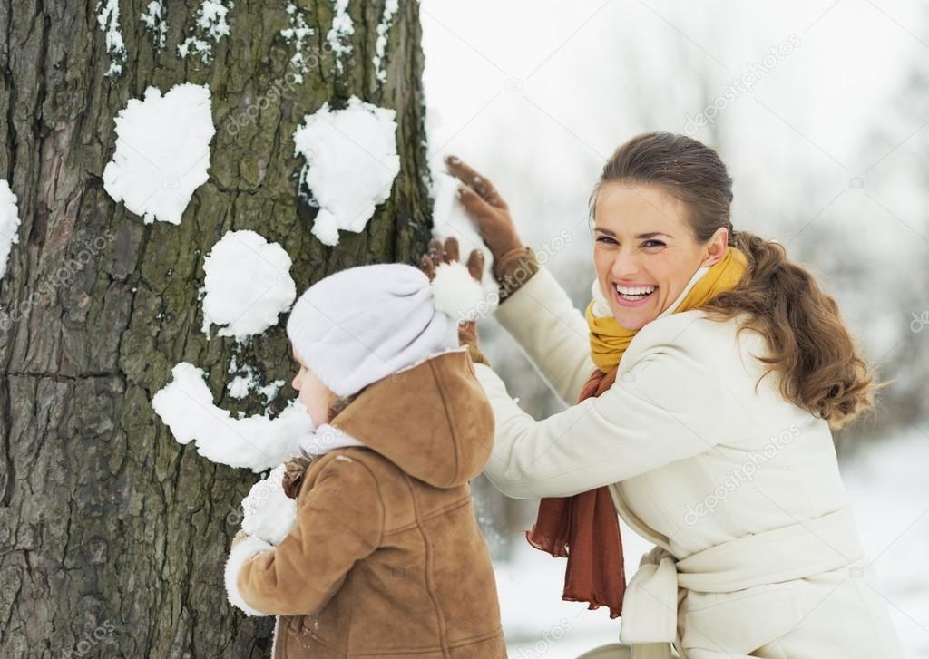 Happy mother and baby making face for tree using snow