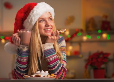 Noel Baba şapkası ile fincan sıcak çikolata ve Noel kurabiyesi düşünceli genç kız