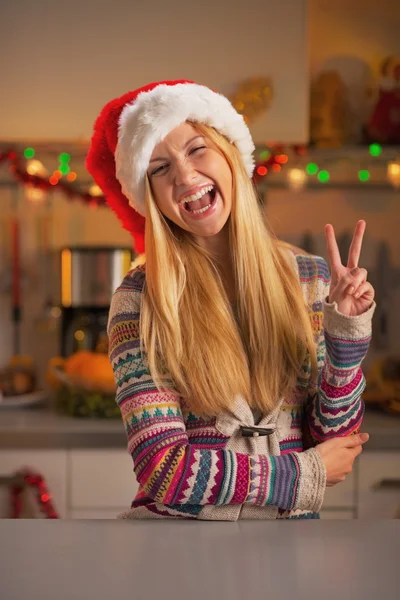 Feliz adolescente en sombrero de santa mostrando gesto de victoria en la cocina decorada de Navidad —  Fotos de Stock