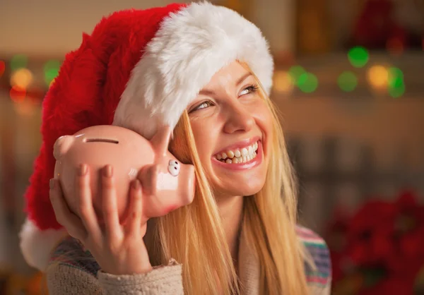 Smiling teenage girl in santa hat shaking piggy bank — Stockfoto