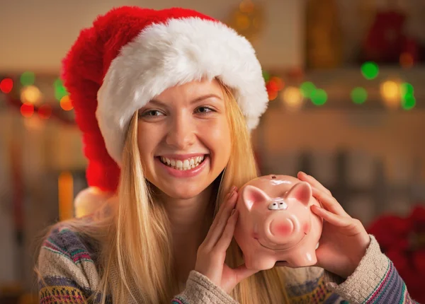Tienermeisje in Kerstman hoed piggy bank in Kerstmis tonen ingericht keuken — Stockfoto