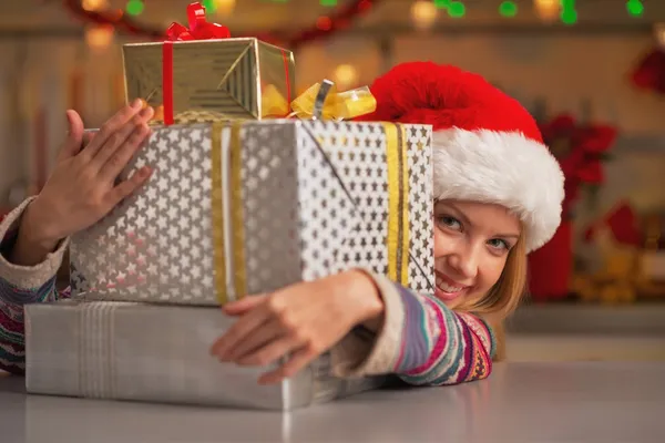 Santa şapka Noel hediye kutuları yığından bakan gülümseyen genç kız — Stok fotoğraf