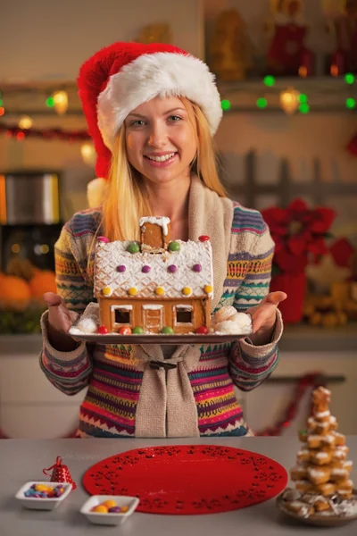 Happy teenage girl in santa hat showing christmas cookie house — Stock Photo, Image