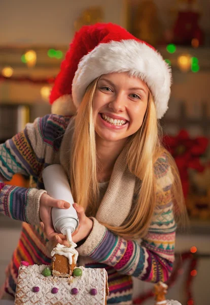 Gelukkig tienermeisje in Kerstman hoed versieren van Kerstmis cookie huis — Stockfoto