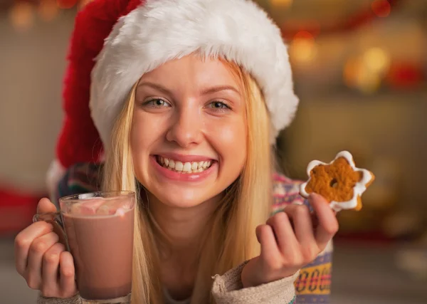 Smiling teenage girl in santa hat with cup of hot chocolate and christmas cookie — Stock Photo, Image