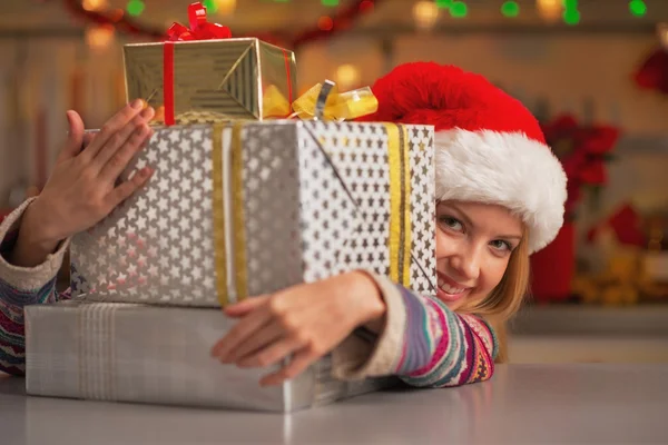 Улыбающаяся девочка-подросток в шляпе Санты, выглядывающая из стопки рождественских подарков Стоковое Изображение
