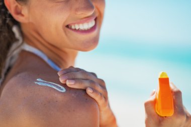 Closeup on happy young woman applying sun block creme clipart