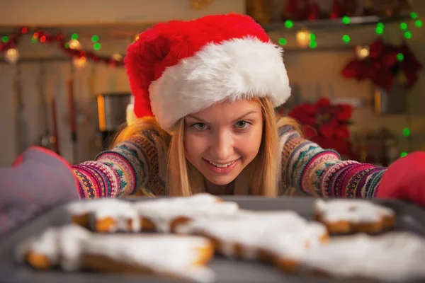 Smiling teenage girl in santa hat pulling out pan of fresh cookies — Stock Photo, Image