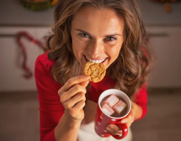 Sorrindo jovem dona de casa comer biscoitos de Natal na cozinha — Fotografia de Stock