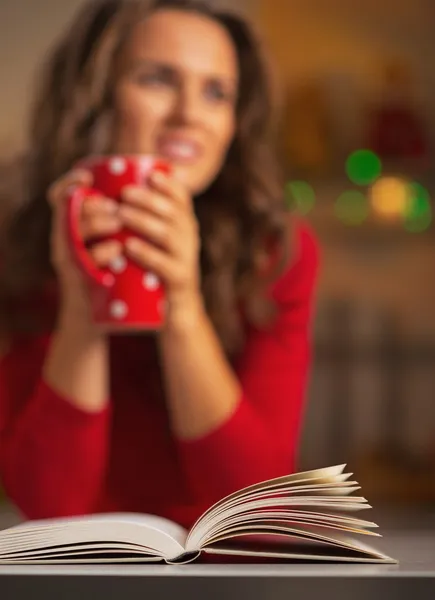 Livro e jovem mulher com xícara de chocolate quente no fundo — Fotografia de Stock