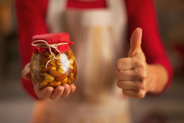 Mladá hospodyňka ukazující sklenici s medovými ořechy a palec nahoru — Stock fotografie