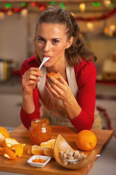 Jonge huisvrouw eten sinaasappeljam in Kerstmis ingericht keuken — Stockfoto