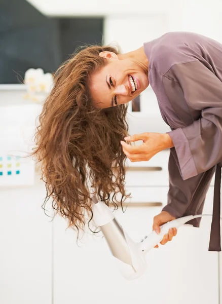 Smiling young woman blow drying hair in bathroom — Stock Photo, Image